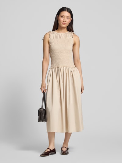 Frauenmodel trägt Midikleid mit Smok-Detail von Comma aus elastischem Baumwoll-Mix in Beige, Taillierte Passform, Rundhalsausschnitt, Ärmelloses-Design, Rückenlänge 128 cm, Brustweite 36 cm, Ganzkörperansicht von vorne.