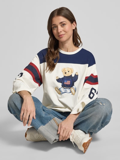 Modelka kobieca nosi Regular Fit Sweatshirt mit Polo-Bear Print von Polo Ralph Lauren, efekt: wzór na całej powierzchni, krój: krój regular fit, aplikacja: nadruk polo bear, dekolt: okrągły dekolt, rękawy: długi rękaw, wykończenie materiału: dzianina dresowa, materiał: czysta bawełna, widok całej sylwetki z przodu.