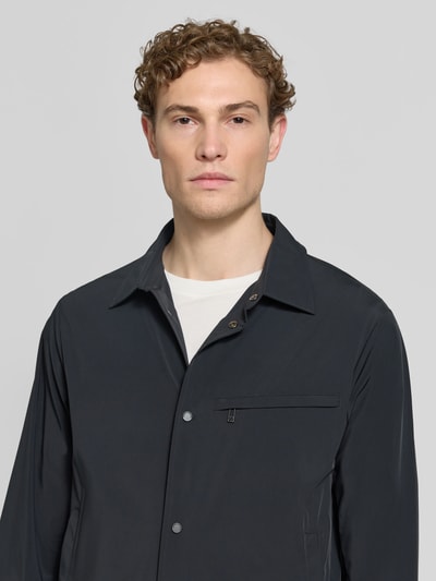 Männermodel trägt Blouson mit Kentkragen und Brusttasche von ARMANI EXCHANGE, dunkle Farbe, glatte Textur, Nahaufnahme Oberkörper. Material-Mix mit Stretch-Anteil, Regular Fit, Knopfleiste, Reißverschluss-Brusttasche.