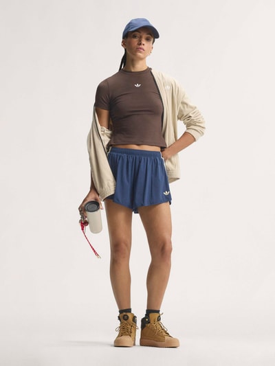 Frauenmodel trägt Loose Fit Sportshorts mit Kontraststreifen von adidas, blau mit weißen Streifen, adidas Training, Ganzkörperansicht von vorne.