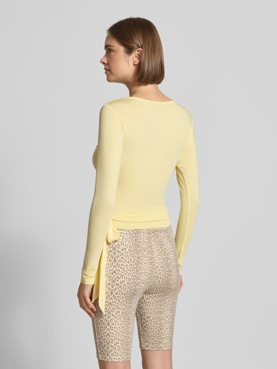 Frauenmodel trägt Cardigan in Wickel-Optik Modell 'Luca' von OH APRIL in Gelb, schmale Passform, Ganzkörperansicht Rückansicht. Modal-Elasthan-Mix, V-Ausschnitt, Rückenlänge bei Größe S 46 cm, kombiniert mit gemusterten Shorts.