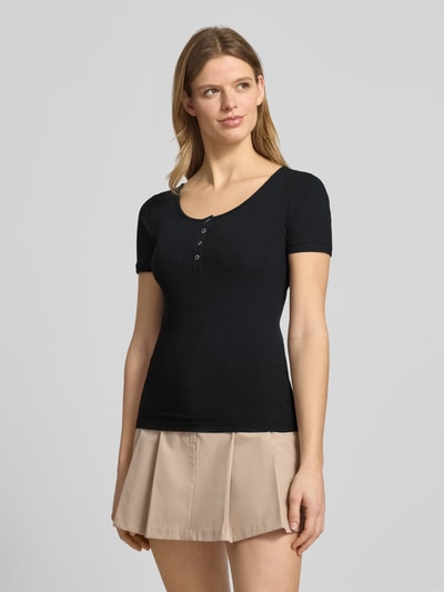 Modelka nosi damski t-shirt Slim Fit T-Shirt aus Baumwoll-Mix Modell 'KITTE' od Pieces, efekt: jednolity kolor, krój slim fit, dekolt w łódkę, henley, rękaw: krótki rękaw, wykończenie materiału: prążkowanie, materiał: mieszanka bawełny, przód, zdjęcie całopostaciowe z przodu.