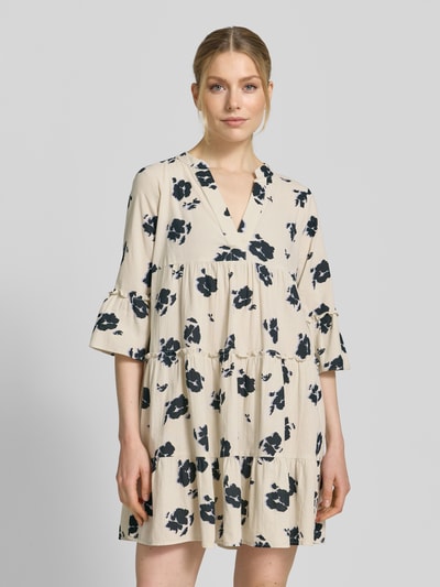 Frauenmodel trägt Ausgestelltes Blusenkleid aus reiner Baumwolle Modell 'DICTHE' von Vero Moda mit Allover-Muster, Henley-Ausschnitt und Trompetenärmeln, cremefarbene Grundfarbe mit dunkelblauen floralen Formen, strukturierte Baumwolltextur, Ganzkörperansicht von vorne.