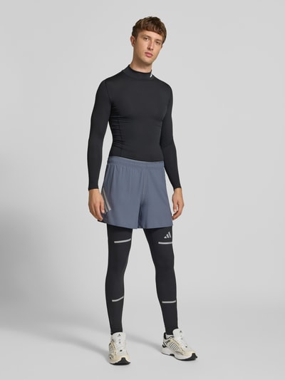 Männermodel trägt Slim Fit Trainingshose mit reflektierenden Details Modell 'adi' von adidas, Farben Schwarz und Grau, adidas Training, Ganzkörperansicht von vorne.