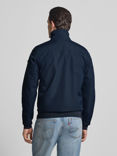 Męski model nosi Regular Fit Kurtka z stójką Model 'Alvin' od Didriksons, granatowy, wpuszczane kieszenie, długość tyłu 69 cm, szerokość ramion 44 cm, szerokość w rozmiarze M 54 cm, długość rękawów 70 cm, widok całej sylwetki z tyłu.
