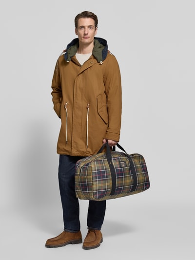 Männermodel trägt Weekender mit abnehmbarem Schulterriemen von Barbour im Karomuster, Ganzkörperansicht von vorne.