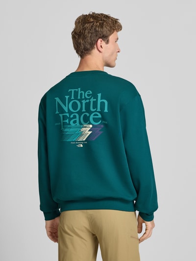 Männermodel trägt Relaxed Fit Sweatshirt aus Baumwoll-Mix von The North Face in Grün, Logo-Print, elastische Abschlüsse, Ganzkörperansicht Rückansicht.
