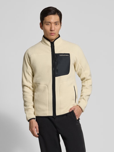 Męski model nosi Jacke mit Teddyfell od PEAK PERFORMANCE, kremowa faktura pluszu, prosty krój, stójka, detal logo, widok całej sylwetki z przodu.