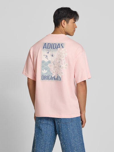 Männermodel trägt Relaxed Fit T-Shirt aus reiner Baumwolle Modell 'SUMMER GRAPHIC' von adidas Originals in zartem Rosa, Ganzkörperansicht Rückansicht. Herren T-Shirt von adidas Originals.