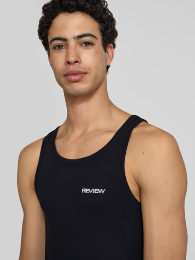 Männermodel trägt Tanktop in Ripp-Optik mit Logo von REVIEW in Schwarz, Slim-Fit aus Reine Baumwolle mit Rundhalsausschnitt, Nahaufnahme Oberkörper.