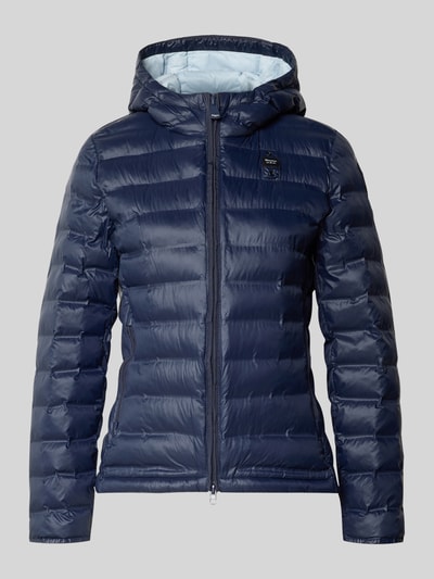 Frauenmodel trägt Steppjacke mit Zweiwege-Reißverschluss Modell 'ELLIS' von Blauer Usa in Dunkelblau, glatte Oberfläche, Ganzkörperansicht von vorne, Slim Fit, Kapuze, Rückenlänge 57 cm, Schulterbreite 35 cm, Brustweite 48 cm, Ärmellänge 60 cm.