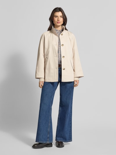 Modelka nosi Relaxed Fit Jacke mit Stehkragen od comma, mieszanka bawełny, wpuszczane kieszenie, stójka, listwa guzikowa, beżowa, widok całej sylwetki z przodu.