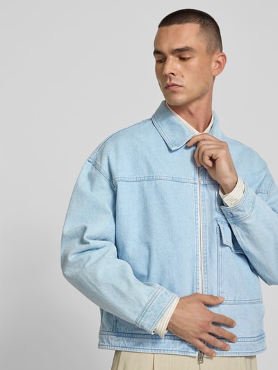 Männermodel trägt Jeansjacke aus reiner Baumwolle von MAISON KITSUNÉ in Hellblau, gerade Passform, Zweiwege-Reißverschluss, Nahaufnahme Oberkörper.