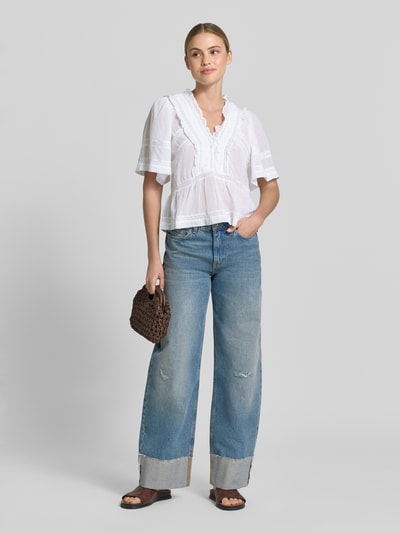 Frauenmodel trägt Blusenshirt mit Häkelspitze Modell 'Evienne' von Neo Noir aus Reine Baumwolle, Taillierter Schnitt, V-Ausschnitt, weiße Farbe, kombiniert mit blauer Jeans, Ganzkörperansicht von vorne.