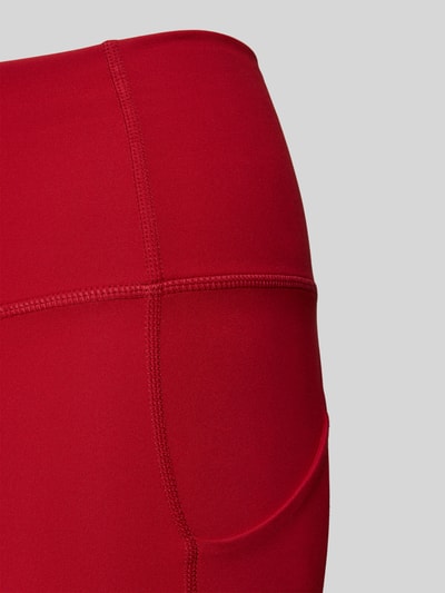 Frauenmodel trägt Slim Fit Leggins mit Beintaschen Modell 'OASIS' von Fabletics in Rot, elastischer Material-Mix, Nahaufnahme Oberkörper.