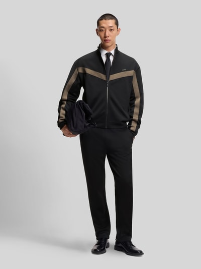 Männermodel trägt Relaxed Fit Jogginghose mit Galonstreifen Modell 'DOLOS' von HUGO in Schwarz, sportliche Sweat-Optik, Ganzkörperansicht von vorne.