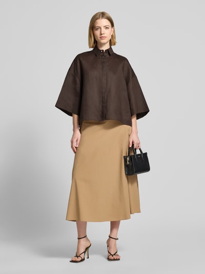 Frauenmodel trägt Boxy Fit Leinenbluse mit 3/4-Arm Modell 'RITO' von MM by Max Mara, Optik: Unifarben, Passform: Boxy-Fit, Kragenform: Hemdblusenkragen, Rückenpasse mit Cacharel-Falte, verdeckte Knopfleiste, 3/4-Arm, Material: reines Leinen, dunkles Braun, glatte, leicht strukturierte Oberfläche, kombiniert mit beigem Rock, Ganzkörperansicht von vorne.