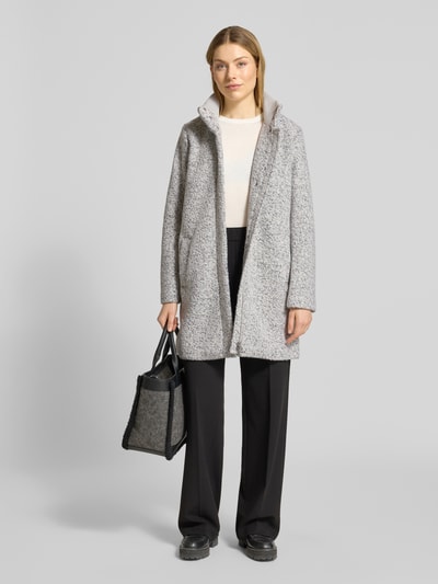 Modelka kobieca ma na sobie Regular Fit Mantel mit Woll-Anteil od Tom Tailor Denim, melanż szary, długi rękaw, tkanina bouclé, widoczne kieszenie wpuszczane, całkowita długość 83 cm w rozmiarze S, szerokość w rozmiarze S 53 cm, szerokość ramion w rozmiarze S 41 cm, długość rękawa w rozmiarze S 62 cm, stójka i kryty dwukierunkowy zamek, widoczny rozporek, widok na całe ciało z przodu.