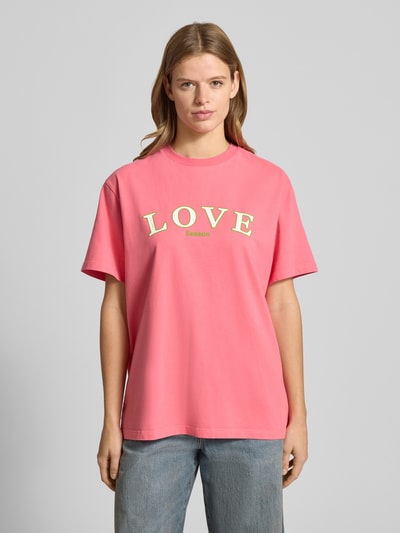 Frauenmodel trägt T-Shirt mit Statement-Print und Rundhalsausschnitt von OH APRIL in Pink, oversized aus reiner Baumwolle, Ganzkörperansicht von vorne.