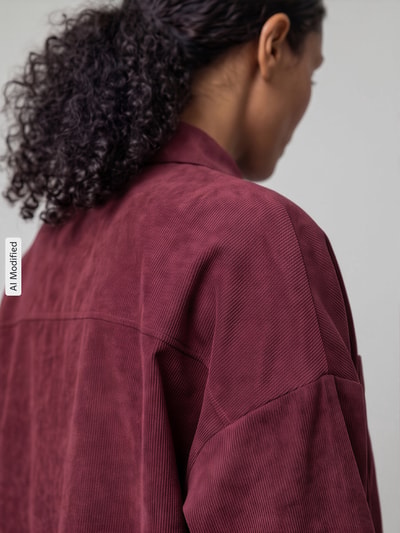 Vrouwenmodel draagt oversized fit blouse met lange mouwen met borstzak model 'SANNE' van VERO MODA, diepe bordeauxrode kleur, detailopname schouderpartij, KI-modificeerd beeld.