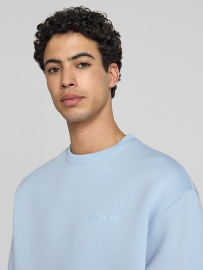 Męskimodel nosi Sweatshirt mit Rundhalsausschnitt und Logo od REVIEW, mieszanka bawełny, krój regular fit, okrągły dekolt, logo, jasnoniebieski kolor, tekstura gładka, długość tyłu w rozmiarze M: 70 cm, długość rękawów w rozmiarze M: 62 cm, zbliżenie na górną część ciała