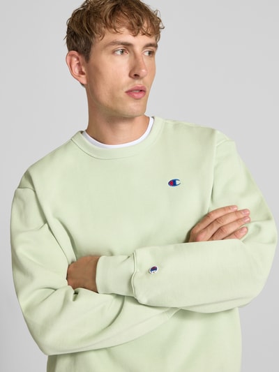 Männermodel trägt Sweatshirt mit Label-Details von Champion in Hellgrün, lockere Passform, Baumwoll-Mix, Nahaufnahme Oberkörper.