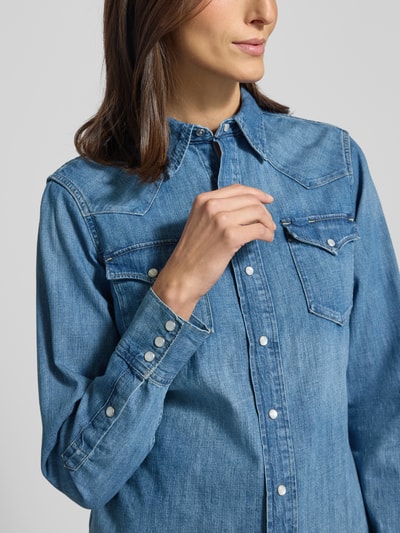Kobiece model prezentuje Regular Fit Jeanshemd mit Brusttaschen od Polo Ralph Lauren z bawełny, niebieska, kieszenie na piersi, listwa guzikowa, kołnierzyk typu kent, krój regular fit, długość tyłu 67 cm, długość rękawów 63 cm, zbliżenie na górną część sylwetki.