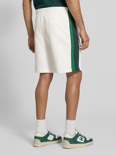 Männermodel trägt Regular Fit Sweatshorts aus reiner Baumwolle von Lacoste in Weiß mit grünen Seitenstreifen, Ganzkörperansicht Rückansicht. Kontext: Herren Sweatshorts von Lacoste