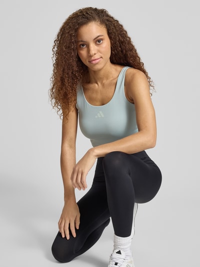 Frauenmodel trägt Slim Fit Sport BH mit Logo-Print von adidas Sportswear in Twist-Optik und Rundhalsausschnitt, helles Uni-Design, Ganzkörperansicht von vorne.