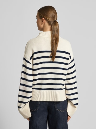 Frauenmodel trägt Regular Fit Pullover aus Woll-Mix Modell 'Sharad' von Lauren Ralph Lauren mit Stehkragen, cremefarben mit dunkelblauen Streifen, breite Abschlüsse, grobe Stricktextur, Rückenansicht, Ganzkörperansicht Rückansicht.