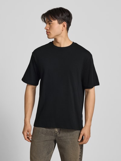 Männermodel trägt Oversized T-Shirt Modell 'FISHER' von Blend, schwarze Reine Baumwolle, Rundhalsausschnitt, Herren T-Shirt, Ganzkörperansicht von vorne. Rückenlänge bei Größe M: 72 cm.