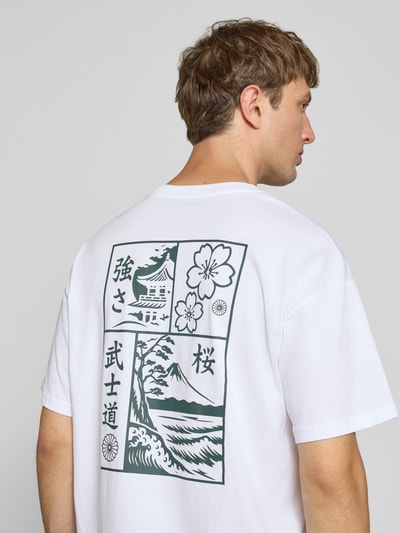 Männermodel trägt Relaxed Fit T-Shirt aus reiner Baumwolle Modell "DYLAN" von JACK & JONES in Weiß mit Print-Detail, Ganzkörperansicht Rückansicht.