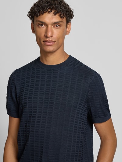Männermodel trägt T-Shirt mit Label-Detail Modell 'Theor' von JOOP! Collection, dunkelblau, Viskose-Mix, strukturierte Oberfläche, Nahaufnahme Oberkörper.