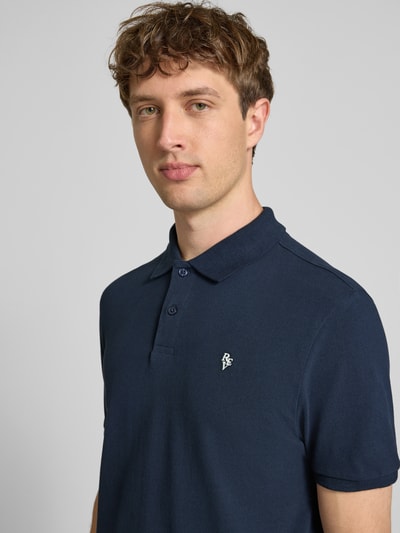 Männermodel trägt Modern Fit Poloshirt mit Logo-Stitching van REVIEW in donkerblauw katoenmix, met polokraag en korte knoopsluiting, ruglengte bij maat M 65 cm, Nahaufnahme Oberkörper.