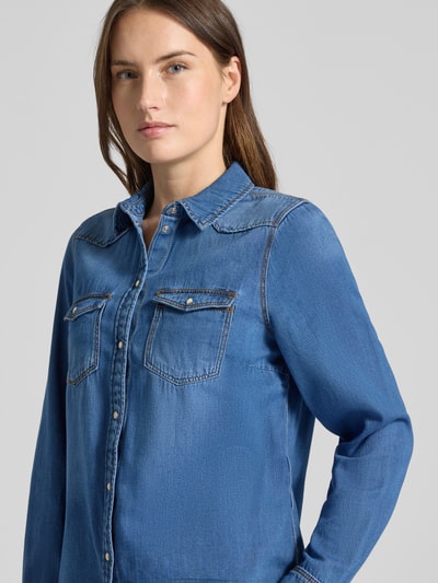 Frauenmodel trägt Regular Fit Jeanshemd aus reiner Baumwolle Modell 'MARIA' von Vero Moda; blaue Denim-Optik, Schmuckknöpfe, Nahaufnahme Oberkörper.