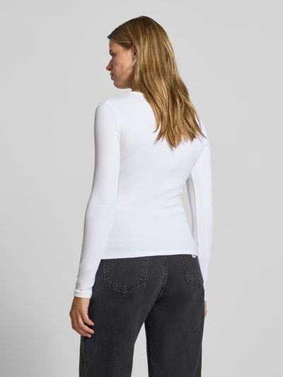 Frauenmodel trägt Slim Fit Langarmshirt aus Baumwoll-Mix von Calvin Klein Jeans, unifarbenes Glattleder, Logo-Applikation aus Metall, Ganzkörperansicht Rückansicht.