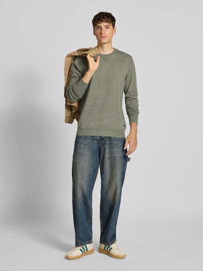Männermodel trägt Strickpullover mit Rundhalsausschnitt Modell 'Bruton' von Blend, gerader Schnitt, Label-Patch, gerippte Abschlüsse, Olivgrün, Ganzkörperansicht von vorne. Rückenlänge bei Größe M 70 cm, Ärmellänge 70 cm.