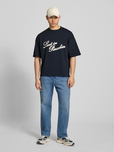 Männermodel trägt T-Shirt mit Logo- und Statement-Stitching von REVIEW, dunkles Blau, Gerader-Schnitt, Reine Baumwolle, Gerippter Rundhalsausschnitt, Herren T-Shirt, Rückenlänge 64 cm, Ganzkörperansicht von vorne.