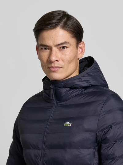 Männermodel trägt Regular Fit Bomberjacke mit down-Füllung von Lacoste, unifarben navy, Kapuzenkragen, Logo-Patch, Nahaufnahme Oberkörper.