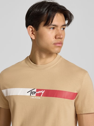 Männermodel trägt Regular Fit T-Shirt aus reiner Baumwolle von Tommy Jeans in Beige mit Label Print, Nahaufnahme Oberkörper.