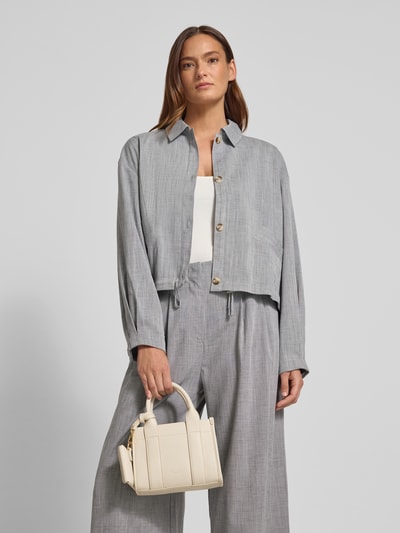 Kobiece modelka ma na sobie szarą marynarkę i spodnie, trzyma Torebka z uchwytem Model 'MELOY MINI TOTE' od Seidenfelt, główna przegroda z zamkiem błyskawicznym, detal z logo, szerokość w rozmiarze 1: 20 cm, długość w rozmiarze 1: 16 cm, głębokość w rozmiarze 1: 8 cm, długość paska na ramię w rozmiarze 1: 108 cm, widok całej sylwetki z przodu.