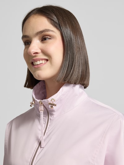 Vrouwenmodel draagt Jacke mit verstellbarem Saum Modell 'Oriella' van JOOP! in lichtroze, met opstaande kraag en tweewegritssluiting, recht model, opgestikte klepzakken, elastische mouwboorden, verstelbare zoom met koordstoppers, ruglengte 61 cm, schouderbreedte 38 cm, borstwijdte 62 cm, mouwlengte 64 cm, detailopname bovenlichaam.