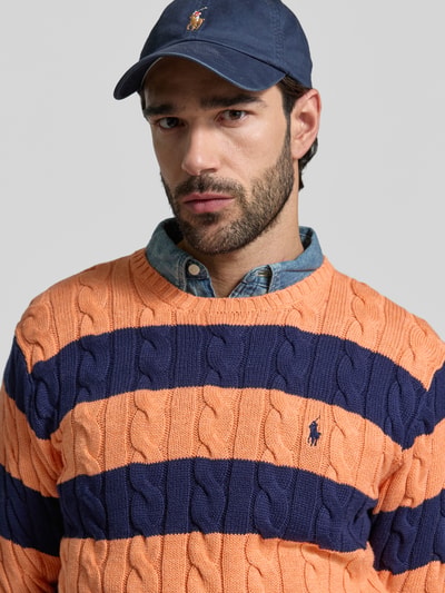 Męski model nosi Regular Fit Strickpullover aus reiner Baumwolle von Polo Ralph Lauren, dwukolorowy, ścieg warkoczowy, detal z logo, imitacja dzianiny, bawełna, okrągły dekolt, długi rękaw, prążkowane wykończenia, całkowite ujęcie górnej części ciała z przodu.