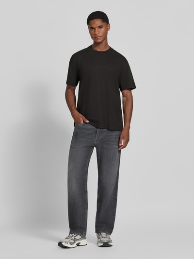 Männermodel trägt Regular Fit T-Shirt aus reiner Baumwolle von Lacoste in Schwarz zu grauen Jeans, Ganzkörperansicht von vorne.