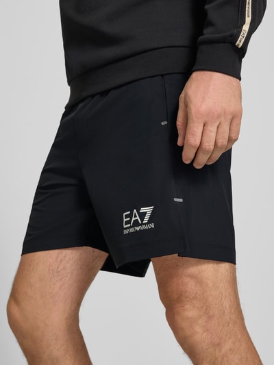 Männermodel trägt schwarze Shorts mit Logo und elastischem Bund von EA7 Emporio Armani, Material-Mix mit Stretch, Nahaufnahme Oberschenkel.