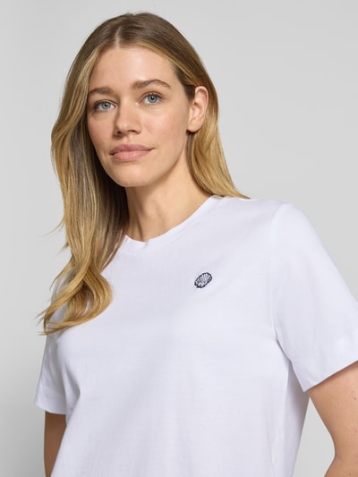 Modelka kobieca ma na sobie Boxy Fit T-Shirt aus reiner Baumwolle Modell 'ELLA' od Selected Femme, jednolity biały kolor, zaokrąglony dekolt, bawełniana tkanina. Zbliżenie na górną część ciała.