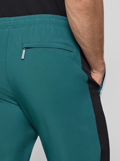 Mężczyzna nosi Sweatpants mit Logo-Stitching Modell 'CASPIO' von SERGIO TACCHINI w kolorze zielonym z czarnymi panelami, z elastycznym pasem i kieszenią, materiał z domieszką stretchu, krój slim fit, detalowe logo, widok z tyłu, zbliżenie na górną część spodni