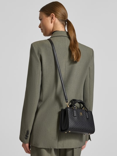 Frauenmodel trägt Henkeltasche mit Allover Logo-Prägung von Tommy Hilfiger in Schwarz mit Logo-Detail und Kunstleder, Ganzkörperansicht Rückansicht.