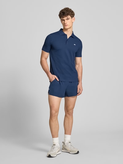 Männermodel trägt Slim Fit Poloshirt mit Logo Modell 'EDMOND' von Ellesse aus Material-Mix mit Stretch-Anteil in Dunkelblau, Ganzkörperansicht von vorne. Herren Poloshirt, Knopfleiste, Rückenlänge bei Größe M: 63 cm.