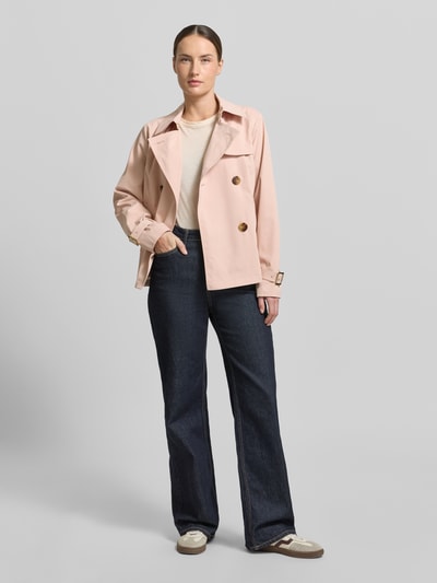 Modelka kobieca nosi Trenchcoat mit Knopfverschluss od MICHAEL Michael Kors, jasnoróżowy, krój regular fit, szerokość w rozmiarze S: 52 cm, długość tyłu 61 cm, szerokość ramion 40 cm, długość rękawa 63 cm, gładka faktura, z dwurzędowym zapięciem i klasycznym kołnierzem, widok całej sylwetki z przodu.